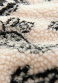 Tekstureret fleece tæppe i blød pink med et sort blomster mønster, der har en fluffig og hyggelig overflade samt tykk pile for varme.