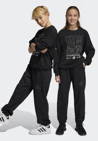 Sudadera negra con estampado gráfico y corte relajado, combinada con pantalones de chándal ajustados a juego. Ambos cuentan con la marca Adidas.