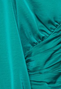 Tessuto di raso teal con una texture liscia, caratterizzato da sezioni arricciate e pieghe asimmetriche, che creano una caduta fluida.