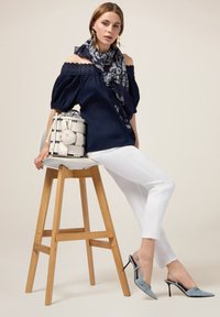 Top navy a spalle scoperte con bordo in pizzo, pantaloni bianchi aderenti, tacchi slingback azzurro chiaro e una sciarpa a fantasia, abbinati a una borsa a righe.