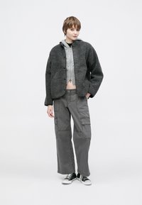 Γκρίζο, αφράτο μπουφάν με κουκούλα, φορεμένο πάνω από ένα ανοιχτογκρίζο cropped πουλόβερ· συνδυασμένο με χαλαρό γκρίζο cargo παντελόνι και μαύρα αθλητικά παπούτσια.