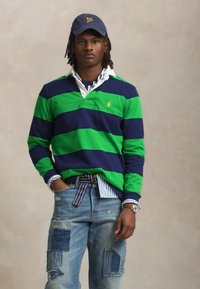 Green and navy striped long-sleeve rugby shirt with a white collar, paired with distressed denim jeans featuring various patchwork details.