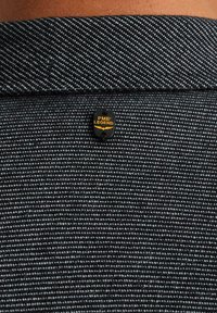 Tessuto a strisce nere e grigie con colletto a polo, dotato di un piccolo tag nero con la scritta "PME LEGEND" in giallo.