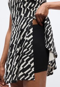 Μπλουζάκι σε ασπρόμαυρο σχέδιο με φαρδιά γραμμή και πλαϊνή σχισμή, συνδυασμένο με μαύρο σορτς. Λείο ύφασμα με ορατές ραφές.
