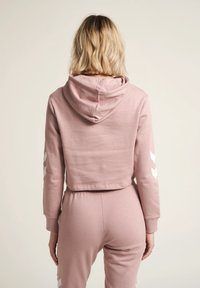 Cappuccio corto rosa chiaro realizzato in tessuto morbido, con cappuccio e strisce a zigzag bianche sulle maniche, cuciture visibili e vestibilità rilassata.