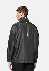 Czarna, lekka kurtka z wysokim kołnierzem, z widocznym żółtym pionowym paskiem z tyłu i elastycznymi mankietami. Gładka faktura.