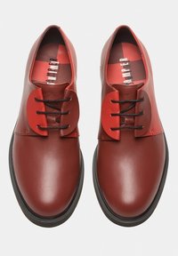 Rote Lederschuhe mit glatter Oberfläche, einzigartigen übergroßen roten Schnürsenkeln und schwarzen Schnürsenkeln. Flache schwarze Gummisohle, minimalistisches Design.