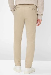 Beige broek met een slim-fit ontwerp, voorzien van twee achterzakken en een gladde textuur. G gedragen met witte sneakers en een lichte trui.