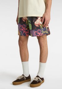 Vícebarevné kraťasy s abstraktními vzory v odstínech fialové, červené a zelené. Nosené s bílými ponožkami a hnědými teniskami.