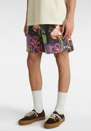 Multikolore shorts med abstrakte mønstre i nuancer af lilla, rød og grøn. Båret med hvide ankelsokker og brune sneakers.