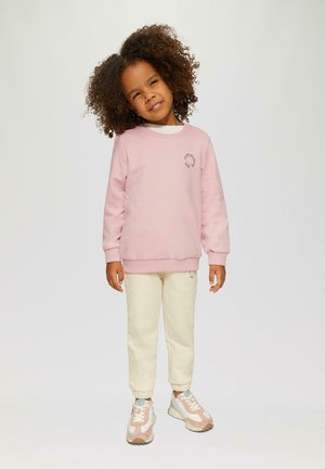 Lichtroze sweatshirt met een ronde geborduurde detail. Crème kleurige joggers met een geborduurde broekspijp. Sneakers met een mix van roze, wit en grijs.