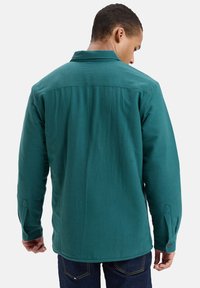 Zielona koszula z długim rękawem, z kołnierzykiem typu spread, mankietami na guziki i prostym dołem. Wykonana z teksturowanej tkaniny o usystematyzowanym wzorze.
