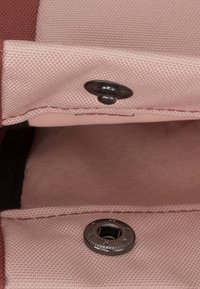 Vaaleanpunainen kangas, jossa on teksturoitu pinta, sisältää kaksi napsulukkosulkua. Sisäosa on näkyvissä, ja se esittelee pehmeän vuorauksen sekä kontrastivärejä.