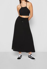 Černý krátký top s tenkými ramínky, který je spárován s černou volnou maxi sukni s elastickým pasem a šňůrkou na stažení. Doplňují ho černé sneakers.