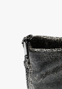 Bolso de piel agrietada en blanco y negro con una superficie texturizada, que presenta un clip de metal negro y un detalle de correa en el borde superior.