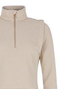 Beige pulovr na zip s vysokým límcem a texturovaným vzorem malých bílých teček. Má dlouhé rukávy a těsný střih.