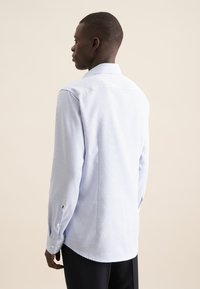 Lichtblauw overhemd met lange mouwen en een subtiel ruitjespatroon, voorzien van een klassieke kraag, gecombineerd met donkere broek.