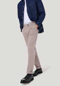 Lichtbeige broek met een rechte pasvorm, voorzien van zijzakken, een knoop aan de voorkant en opgerolde manchetten, gecombineerd met een donkerdenim overhemd en zwarte schoenen.