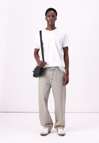 Tricou alb cu mânecă scurtă, blugi largi de culoare albastru deschis, geantă neagră tip crossbody, adidași albi și gri. Outfit simplu și casual.