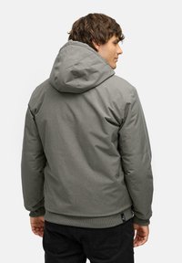 Grå hættejakke med en glat tekstur, elastiske manchetter og kant. Minimalistisk design med et mærke på undersiden, der præsenterer en enkel silhuet.