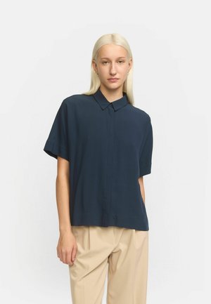 Navy short-sleeve shirt with a button-up collar, featuring a smooth texture and a relaxed fit. Paired with light beige trousers.