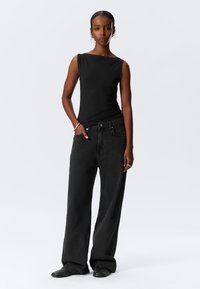 Top negru fără mâneci, cu un decolteu ușor în formă de barcă, asortat cu blugi negri largi. Prezintă o textură netedă și un design minimalist.