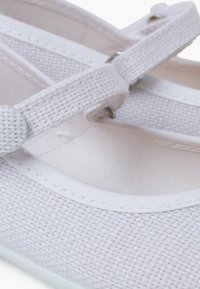 Weiße Ballettschuhe aus Leinen mit einer strukturierten Oberseite, flacher Sohle und einem dünnen Riemen mit einer Metallschnalle für sicheren Halt.