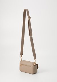 Sac bandoulière rectangulaire beige avec une sangle en tissu réglable et une poche zippée à l'avant avec tirette en métal doré.