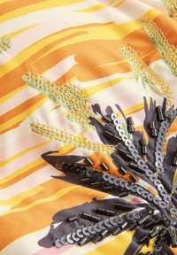 Többszínű szövet, amely absztrakt mintázattal rendelkezik sárga és barna színekben, flitterekkel díszítve és arany színű textúrált öltés részletezéssel.