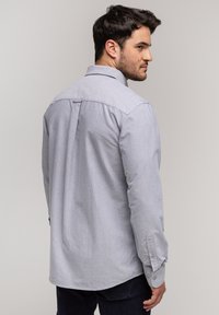 Jasnoszara koszula zapinana na guziki, wykonana z miękkiego materiału, z yoke z tyłu, długimi rękawami i mankietami zapinanymi na guziki, o zaokrąglonym dolnym wykończeniu.