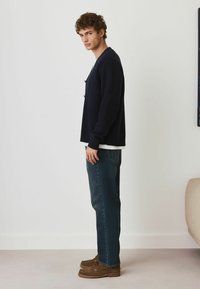 Marinblå stickad cardigan med avslappnad passform, matchad med mörkblå jeans och bruna loafers. Outfiten fullbordas med en vit T-shirt under.