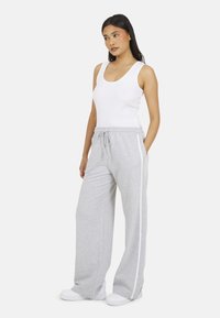 Grijze, wijde sweatpants met een trekkoord in de taille, witte zijstrepen en een zachte textuur, gecombineerd met een witte, fitted tanktop.