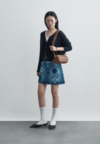 Jeanskjol med diamantmönster, marinblå cardigan, vit topp, svarta spetsiga skor, vita ankelsockor och en brun axelväska.