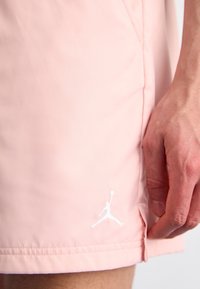 Närbild av en hand som vilar bredvid ljusrosa shorts med en vit Jumpman-logga nära fållen.