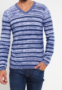 Blå och ljusblå randig långärmad v-ringad tröja med en strukturerad stickning, ribbade ärmslut och nederkant, iklädd denimjeans.