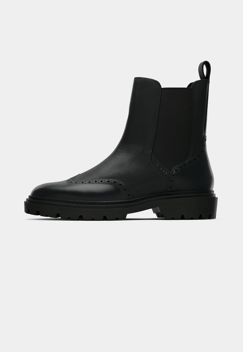 Schwarze Leder Stiefelette mit elastischen Seitenpaneelen, dekorativen Perforierungen und einer robusten Gummisohle. Mit einer Schlaufe am Hinterteil.