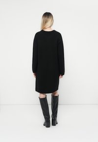 Abito a maglia nero oversize con maniche lunghe, in materiale testurizzato e scollatura rotonda, abbinato a stivali neri fino al ginocchio.