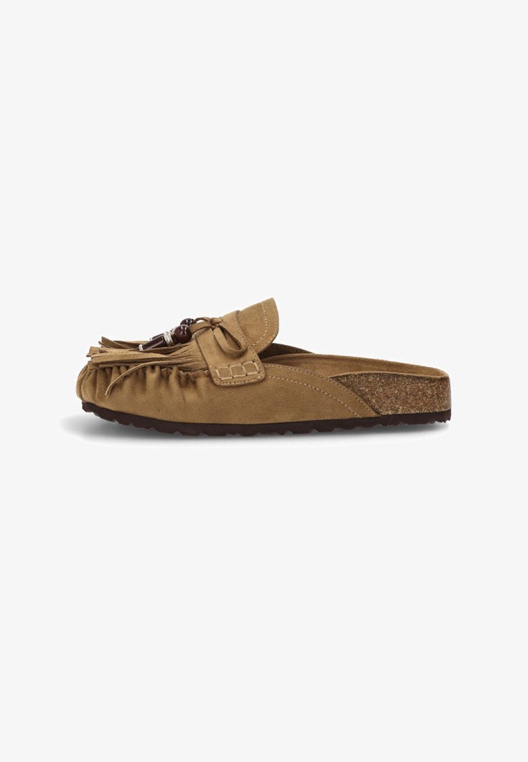 Mocasines de ante marrón sin cordones, con flecos y detalle de lazo, que cuentan con una plantilla de corcho y suela de goma texturizada para un mejor agarre.