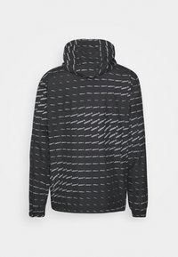 Černá větrovka s kapucí, zdobená opakujícím se vzorem bílého loga. Hladká textura, elastické manžety a nastavitelný stahovací šňůr na kapuci.