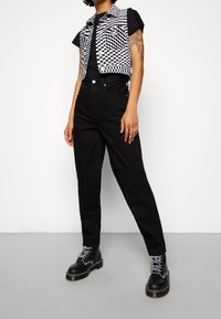 Jeans neri a vita alta abbinati a una t-shirt nera e un gilet a quadri senza maniche. Stivaletti neri con lacci completano il look.