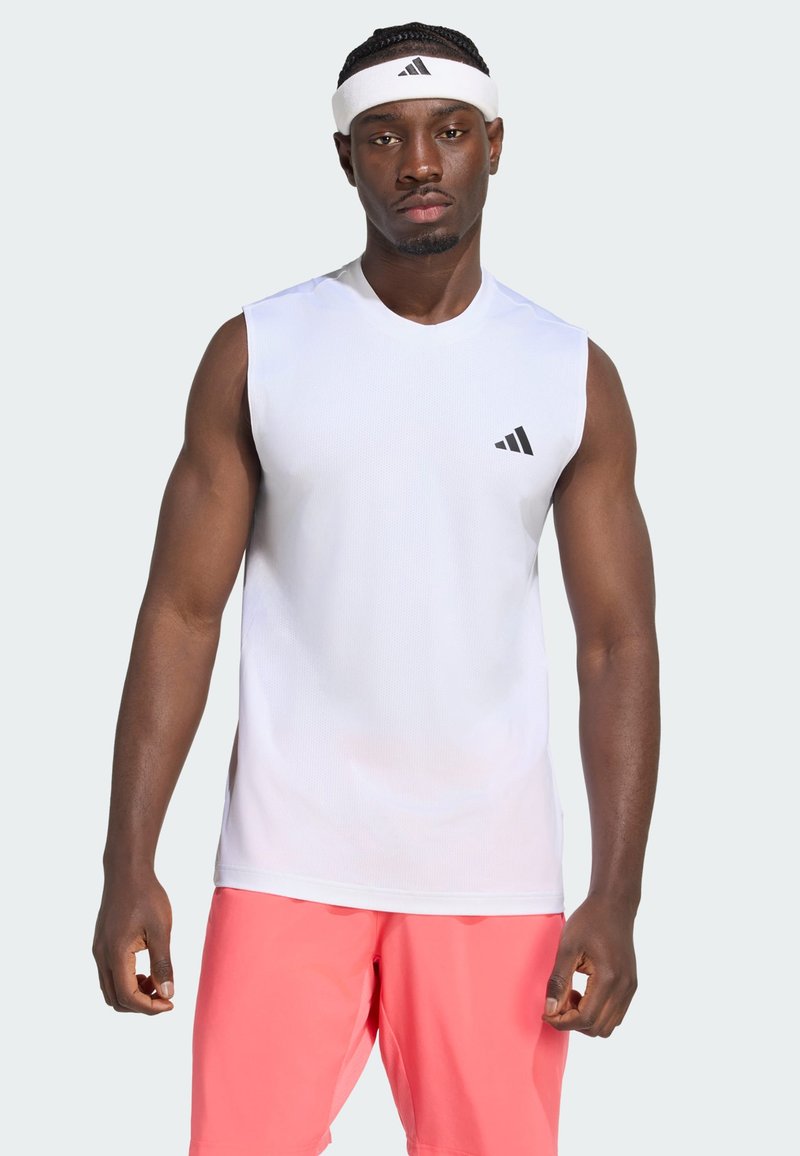 Αθλητής φοράει λευκό αμάνικο μπλουζάκι Adidas, λευκή κορδέλα κεφαλής Adidas και κοραλλί σορτς, στέκεται με ουδέτερη έκφραση και είναι αντικριστά.