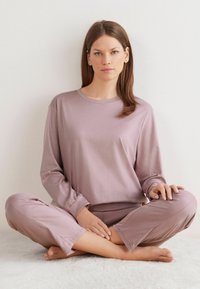 Conjunto de lounge de un suave color malva claro que incluye una camiseta de mangas largas y pantalones ajustados, confeccionado en una tela suave y lisa, con un corte relajado y puños en las mangas.