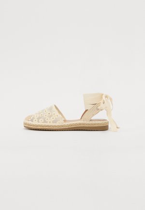 Sandale espadrille beige avec dessus en mesh brodé de marguerites, semelle en jute tressée et fermeture lien à nouer à la cheville sur fond blanc uni.