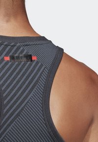Top de entrenamiento negro con rayas grises verticales, que presenta un acento y etiqueta roja en el escote trasero. Material suave y texturizado.