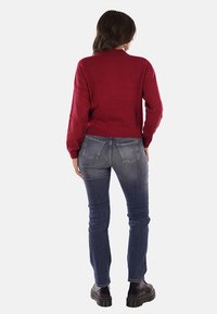 Maglione rosso corto in maglia testurizzata, abbinato a jeans in denim blu con tasche posteriori. Stivaletti neri stringati completano l'outfit.