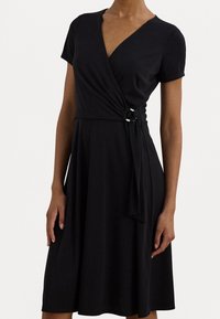 Zwart wikkeljurk met korte mouwen, een V-halslijn en een geknoopte taille. Gemaakt van zachte stof met een vloeiende rok.