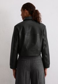 Czarna skórzana kurtka typu cropped o gładkiej fakturze i minimalistycznym designie. Posiada stójkę i długie rękawy, noszona na szare szerokie spodnie.