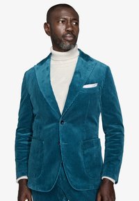 Teal corduroy bleiseri, jossa on nahanet johtavat, kaksi etutaskua ja yksi rintatasku. Päällä teksturoitu kerma turtleneck villapaita.