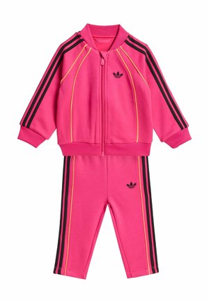 Tuta da ginnastica rosa composta da giacca con zip e pantaloni, con accenti a strisce nere e gialle e un piccolo logo nero su ogni pezzo.