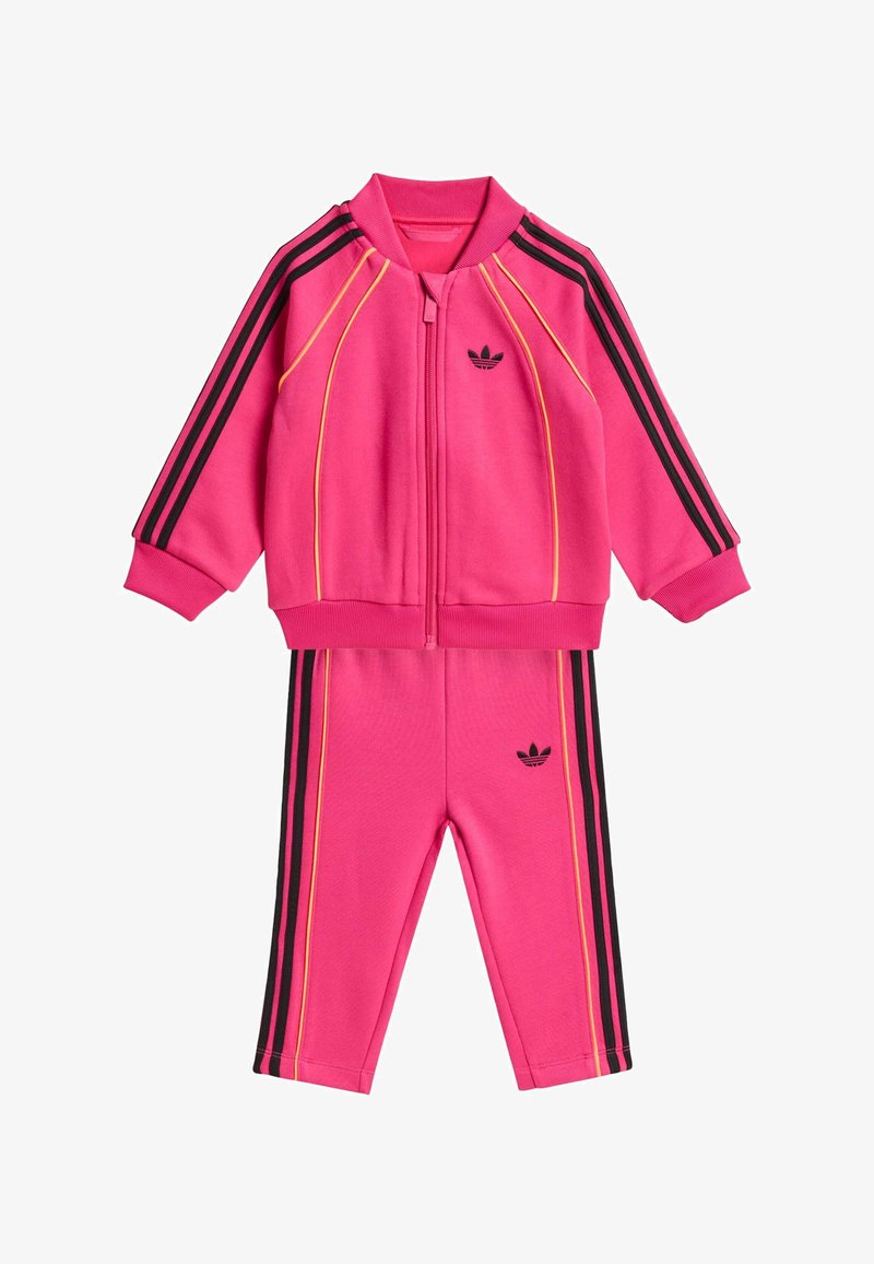Rosa sportliches Trainingsanzug-Set mit Reißverschlussjacke und Hose, versehen mit schwarzen und gelben Streifenakzenten sowie einem kleinen schwarzen Logo auf jedem Teil.